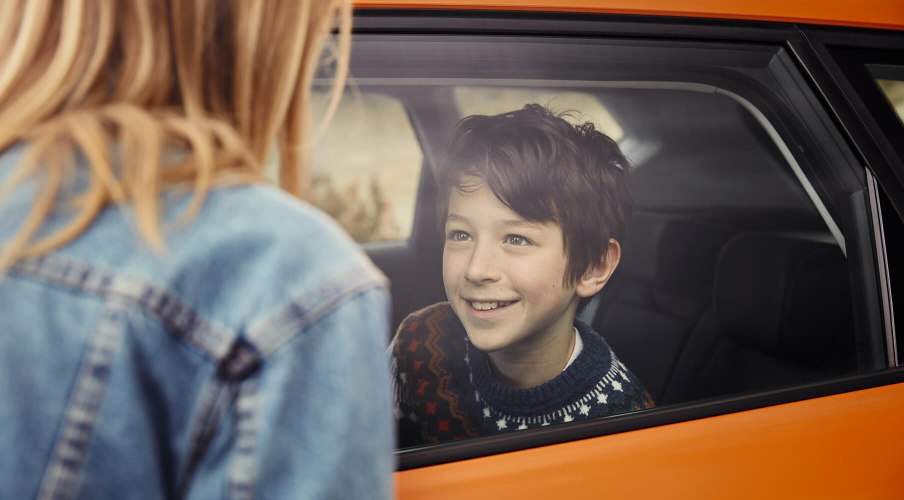 Servizi e manutenzione per vetture nuove SEAT – Un ragazzo in un’auto nuova sorride a una donna in piedi all’esterno, vista laterale