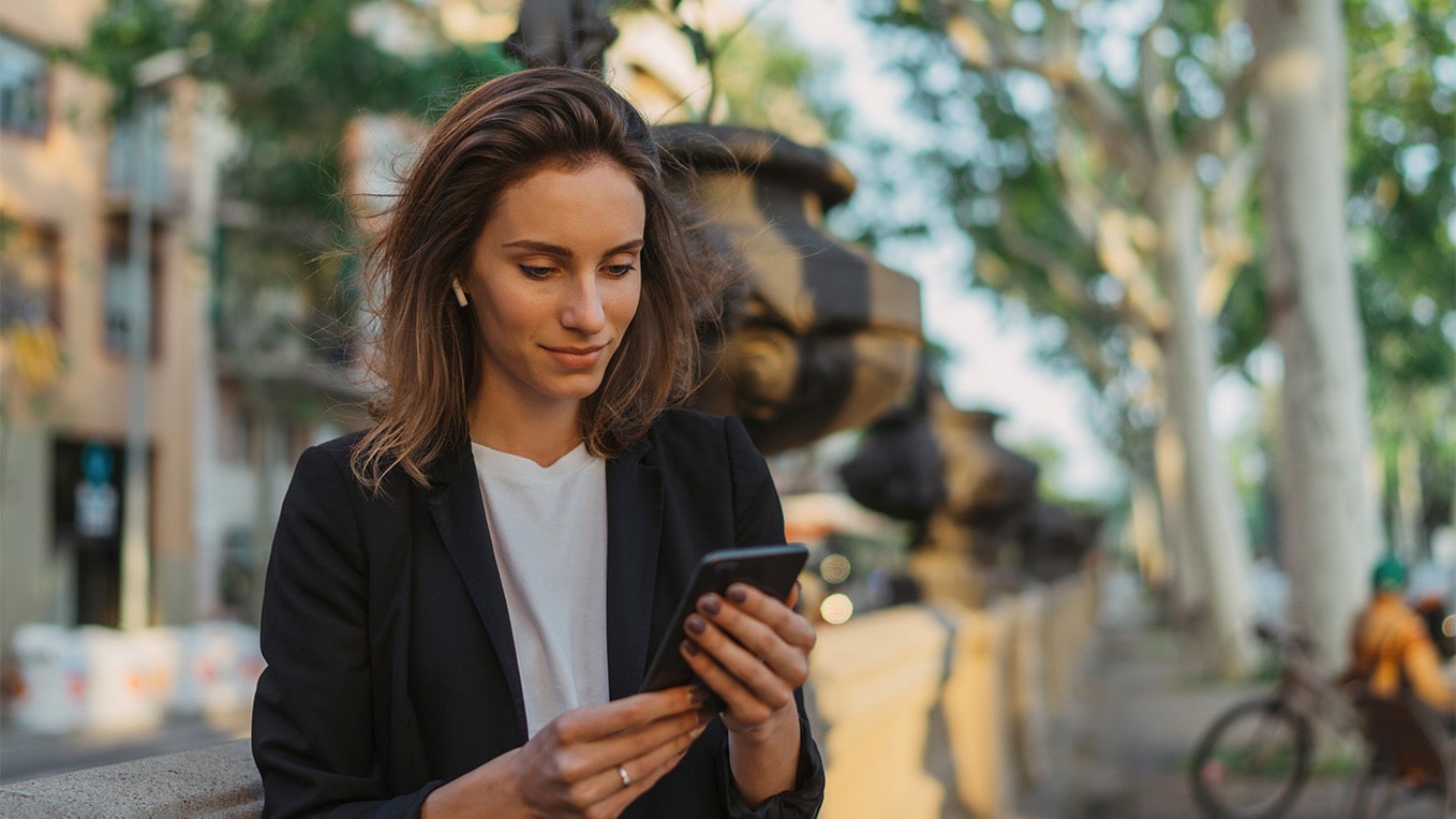 Donna che usa la funzione Seat Connect con il telefono cellulare, mentre è appoggiata contro un muro di cemento nel centro della città.