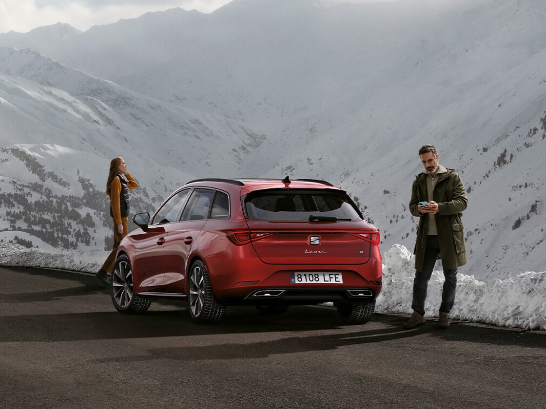 Un’auto SEAT Leon Sportstourer rossa parcheggiata su una strada di montagna in attesa dei vantaggi del servizio mobilità SEAT e del servizio di assistenza stradale. Due persone nelle vicinanze.