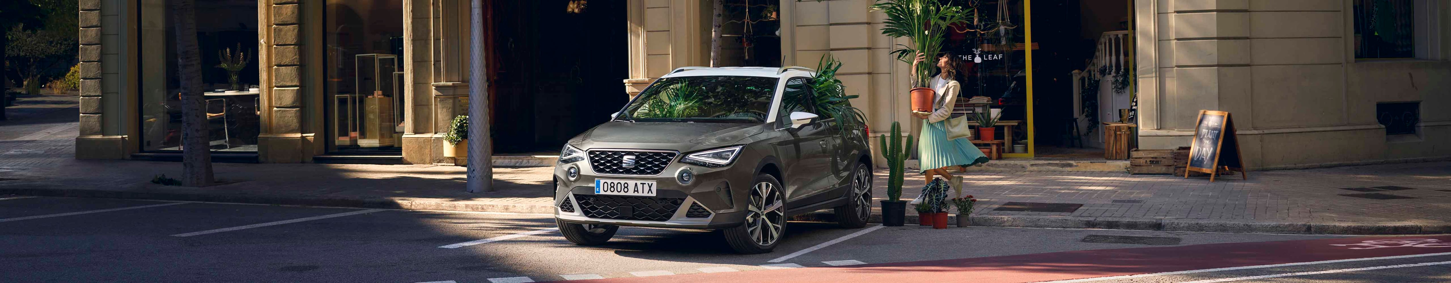 Woman with a plant walking to SEAT arona dark camouflage colour