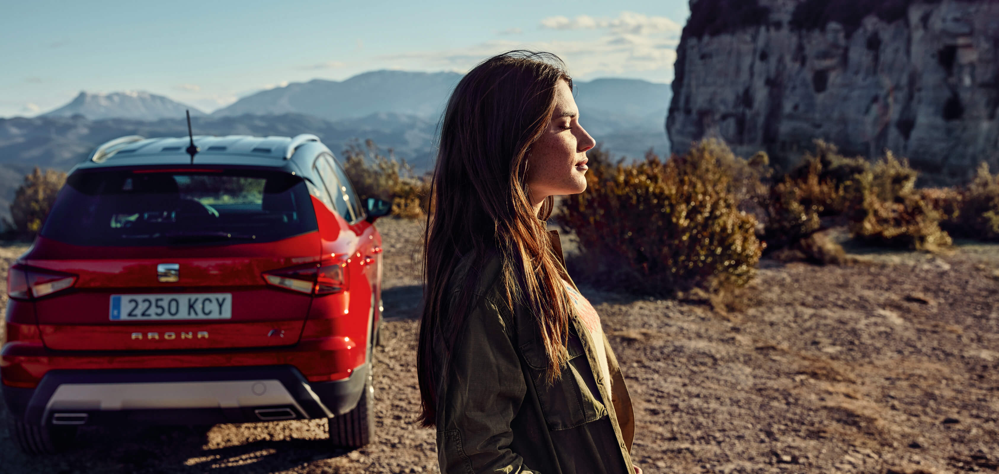 Servizi SEAT per vetture nuove – vista posteriore di un SUV crossover SEAT Arona parcheggiato in un deserto con un profilo di donna