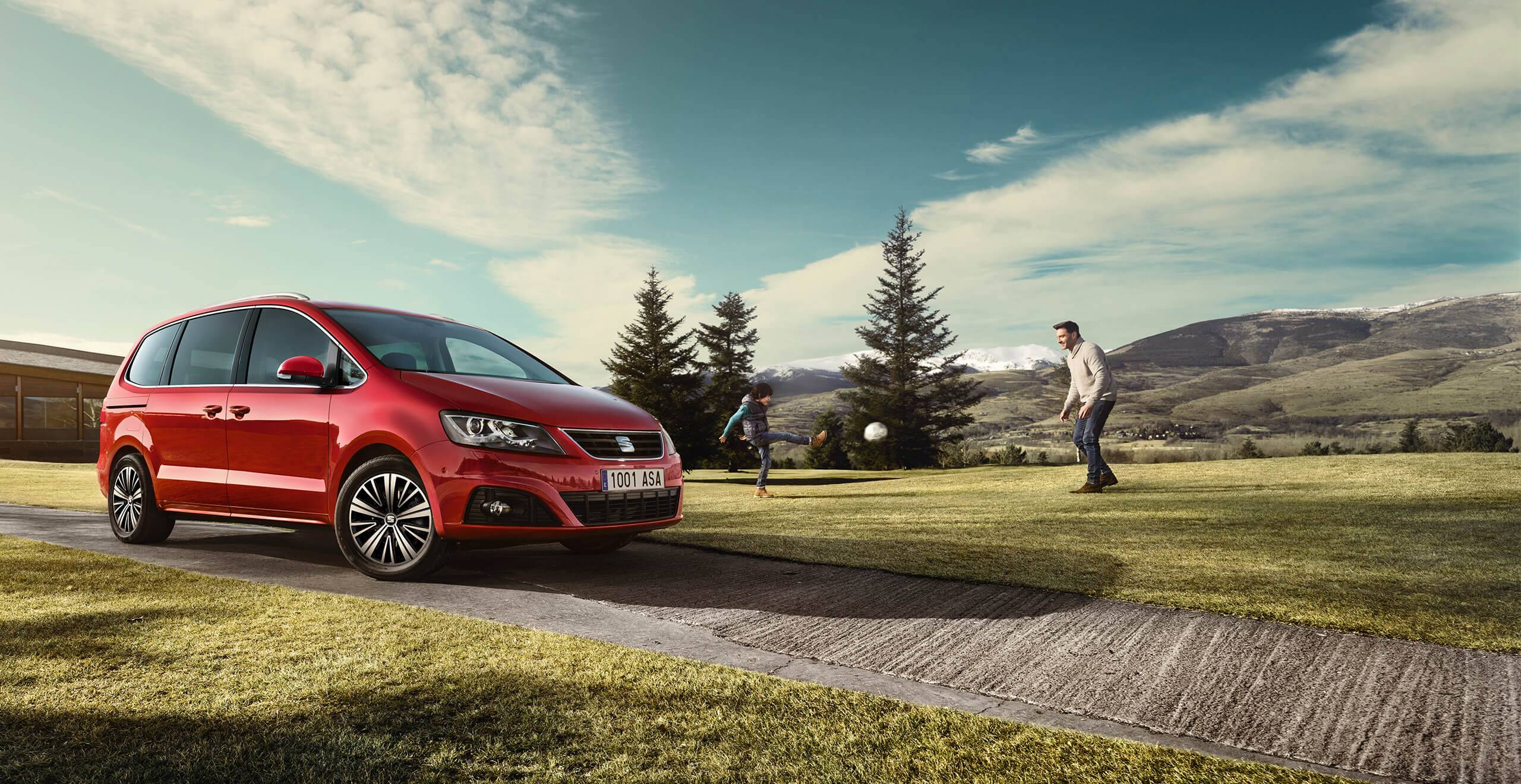 Manutenzione ed estensione di garanzia per vetture nuove SEAT – vista scenica di un monovolume SEAT Alhambra 7 posti rosso con due persone che giocano a calcio sullo sfondo